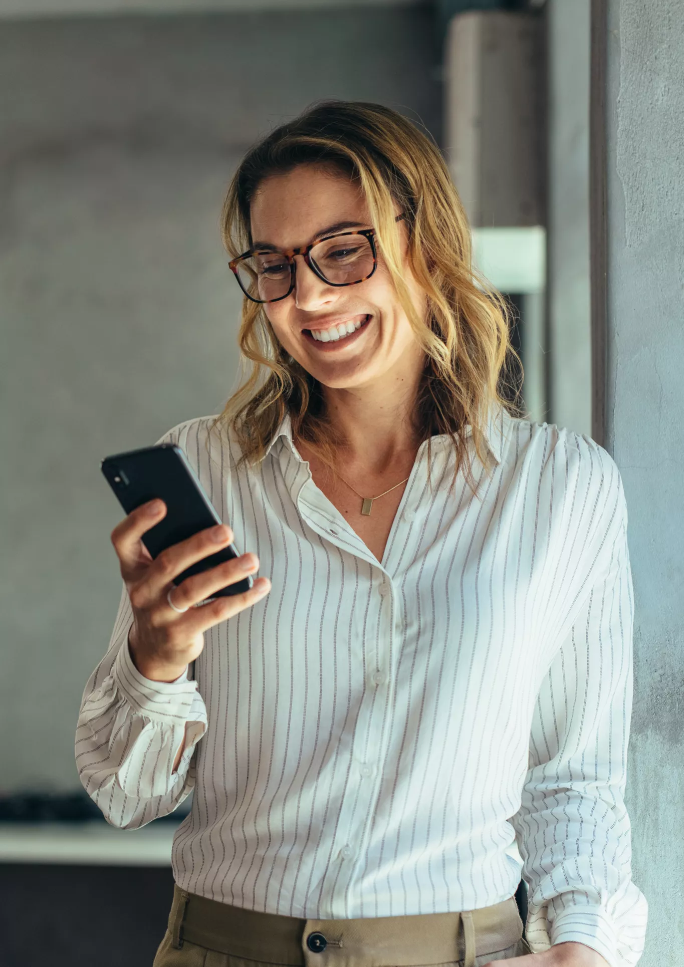 A woman with glasses smiling at her mobile phone